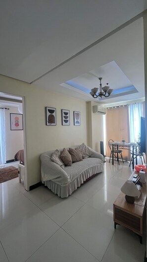 A living room with a sofa, a coffee table, and a dining area with chairs. - JFS Cozy 1-bedroom Staycation in beautiful Manila - Near US Embassy (Manila)