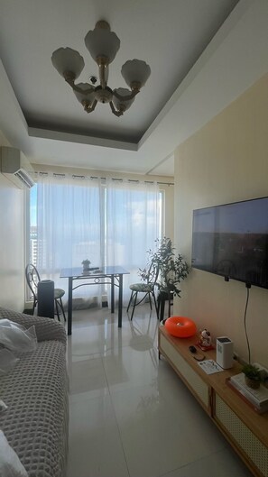 Una sala de estar moderna con un televisor de pantalla plana montado en la pared, un comedor con mesa y sillas, un sofá y un ventilador de techo.