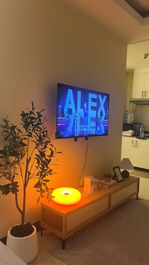 Televisor de pantalla plana montado en una pared mostrando el nombre 'ALEX' con un subtítulo.