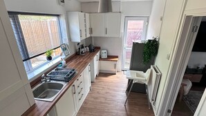 A compact kitchen with a built-in washing machine, a window with blinds, and a view of the outside. - House Sleeps 4 with Patio (Warwick)