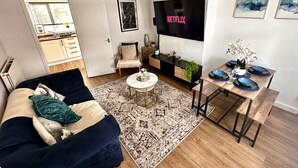 A modern living room with a sofa, coffee table, TV, and a dining area with a table and chairs. - House Sleeps 4 with Patio (Warwick)