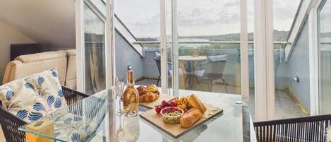 En balkon med et glasbord dækket med mad og drikkevarer, en stol og en sofa.