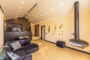 A modern living room with a sofa, a fireplace, and a kitchen area in the background. - Nature Cabin with Spa Jacuzzi Steam Room (El Carmen de Viboral)