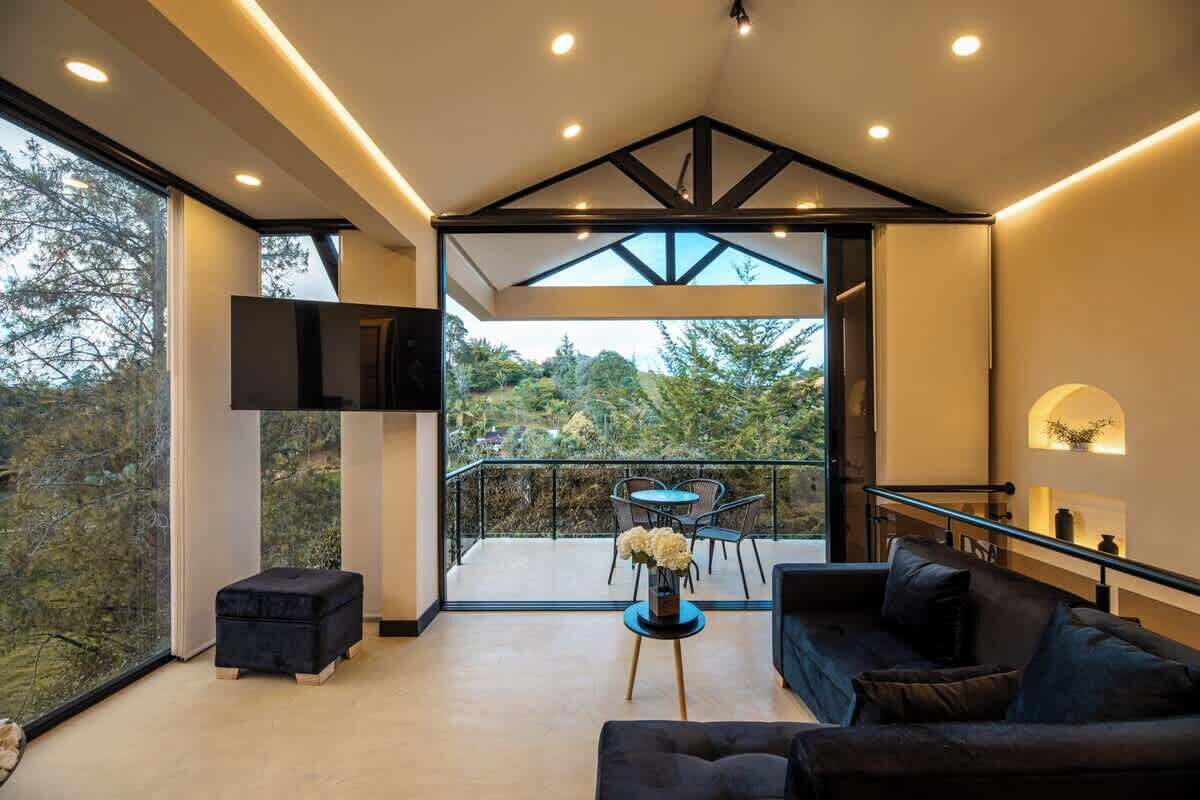 A modern living room with a sofa, a small table with flowers, a TV, and a balcony with a table and chairs.