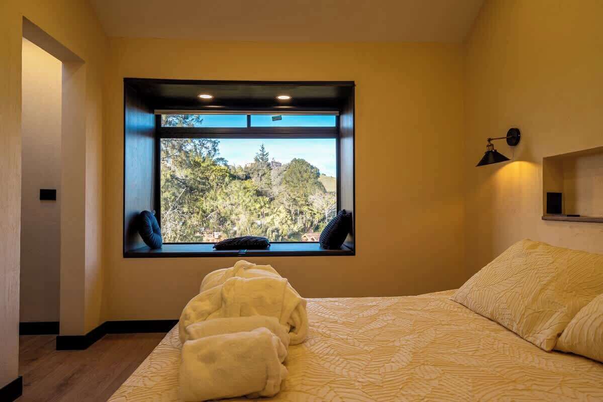 A bedroom with a large window, a bed with a patterned bedspread, and a bedside lamp.