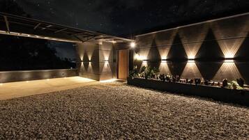 Una terraza al aire libre con suelo de grava, un edificio moderno con iluminación geométrica y un cielo nocturno.