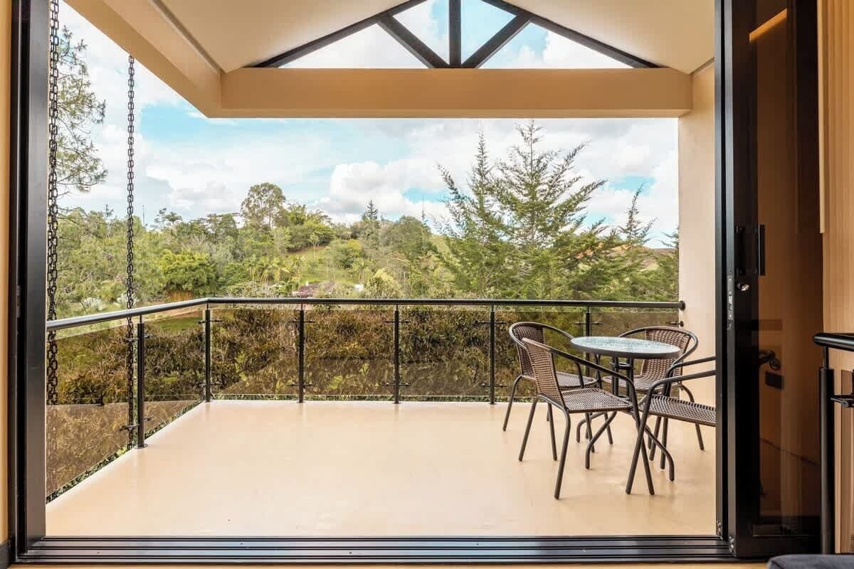 A balcony with a glass door, a table with chairs, and a view of a green landscape.