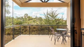 A balcony with a glass door, a table with chairs, and a view of a green landscape.