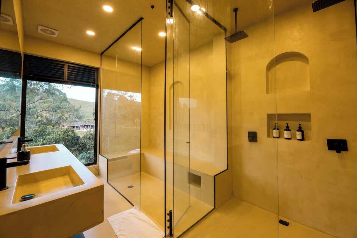 Un baño moderno con cabina de ducha acristalada, un ventanal grande y un lavabo con espejo.