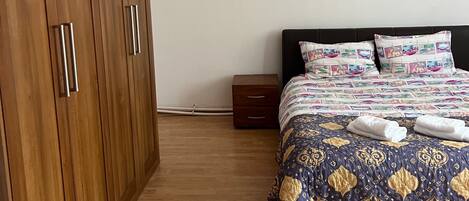 A bedroom with a wooden wardrobe, a bed with patterned bedding, and a bedside table.