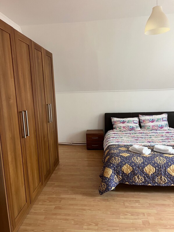 A bedroom with a wooden wardrobe, a bed with patterned bedding, and a bedside table.