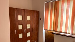 A bedroom with a wardrobe, a bedside table, and a window with striped curtains.