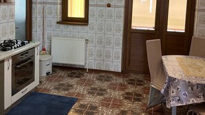 A kitchen with a gas stove, a white radiator, patterned tiles, a window with blinds, and a dining area with a table and chairs.