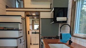 A modern kitchen with a built-in stove, a wooden countertop, and a window with a towel hanging on the door handle. - Nicholson Tiny Home with Hot Tub & Mountain Views (Golden)