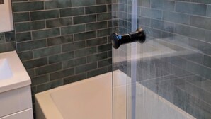 A bathroom with a glass shower enclosure, a white bathtub, and a tiled wall. - Nicholson Tiny Home with Hot Tub & Mountain Views (Golden)