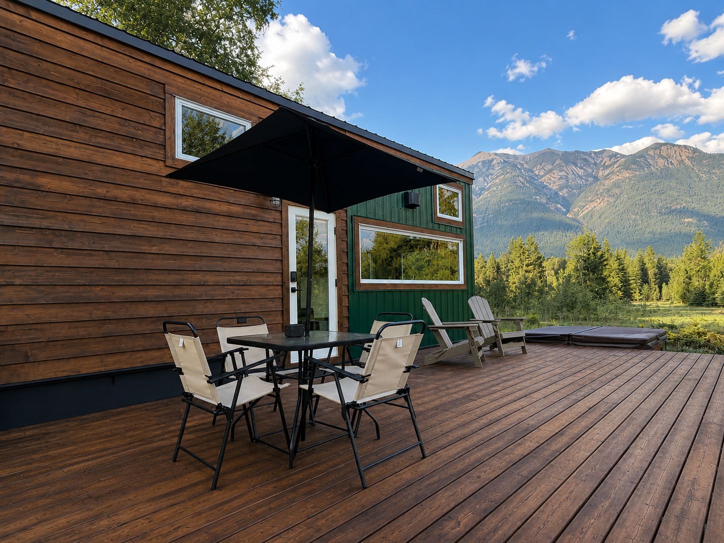 Een houten terras met een tafel en stoelen, een overdekt gedeelte met een parasol en uitzicht op bergen.
