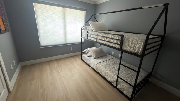 Ein Zimmer mit Etagenbett, einem Fenster mit Jalousien und einem Deckenventilator.
