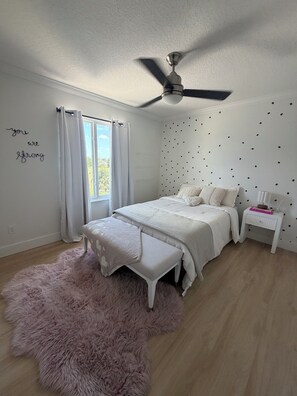 A bedroom with a bed, a bench, a nightstand, a ceiling fan, and a wall with a motivational quote. - Luxurious modern estate minutes from Disney (Davenport)