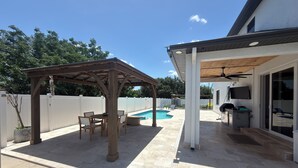 Ein überdachter Patio-Bereich mit Pool, Sitzgelegenheiten im Freien und Grill.