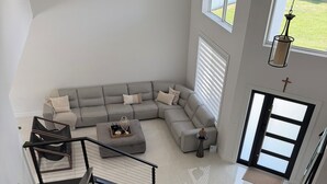 Ein großzügiger Wohnbereich mit einer großen, L-förmigen Couch, einem kleinen runden Tisch und einer Treppe, die zu einer oberen Etage führt.