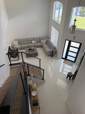 A spacious living area with a large L-shaped sectional sofa, a small round table, and a staircase leading to an upper floor. - Luxurious modern estate minutes from Disney (Davenport)