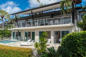 A modern two-story house with a balcony, a swimming pool, and lush greenery.