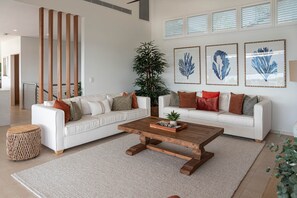 A modern living room with two white sofas, a wooden coffee table, and a large potted plant.