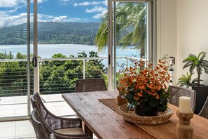 A dining area with a view of a body of water and hills, featuring wicker furniture and a wooden table.