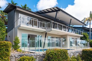 A modern two-story house with a balcony, large glass windows, and a stone retaining wall.
