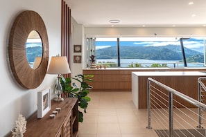 A modern interior with a large mirror, a wooden console table with a lamp, and a view of a lake and forest.