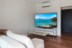 A living room with a flat-screen TV mounted on a white entertainment unit, a brown sofa, and a wooden floor.