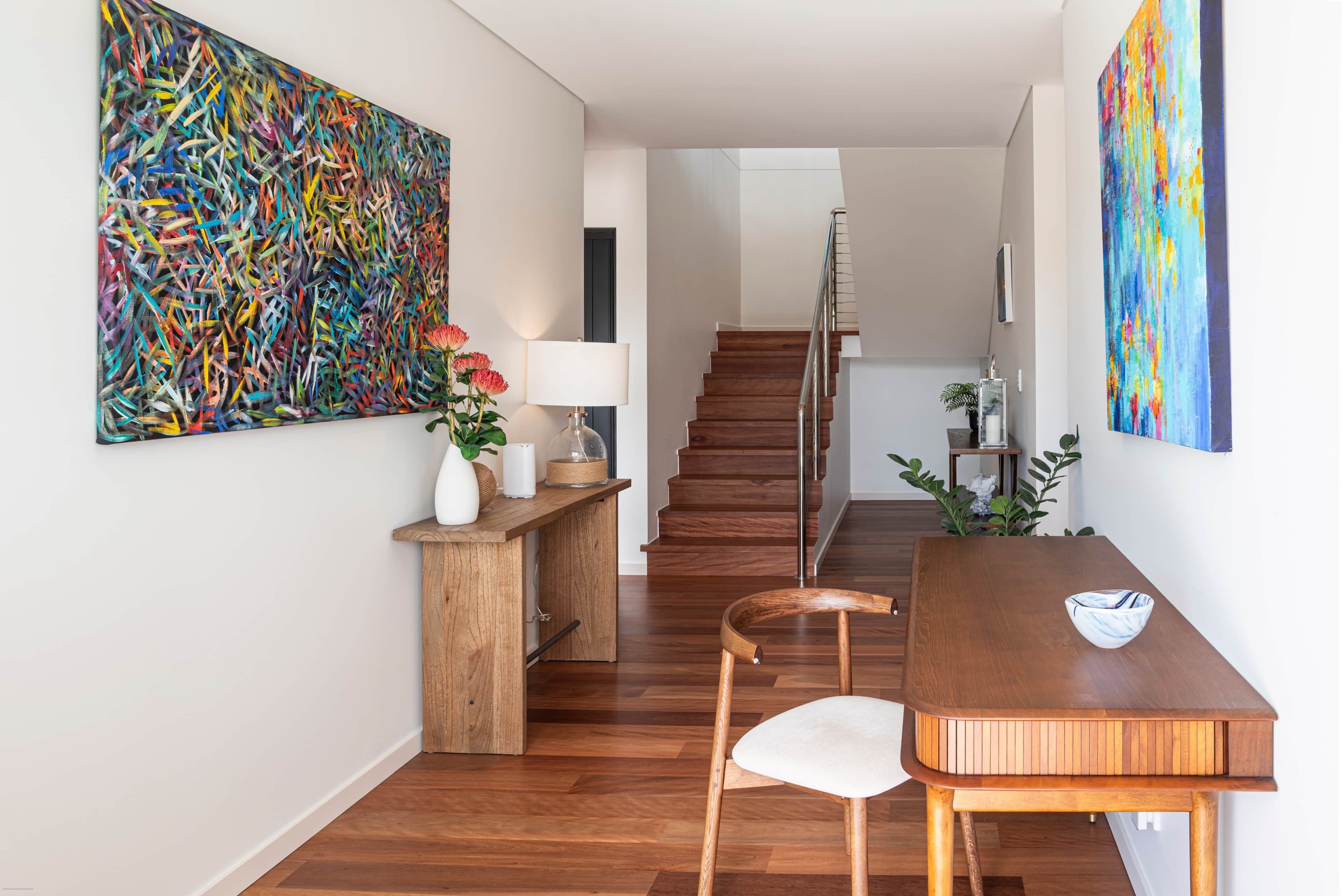 Ein modernes Interieur mit einem Holzes Esstisch, Stühlen, einer Treppe und abstrakten Bildern.