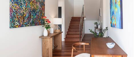 A modern interior with a wooden dining table, chairs, a staircase, and abstract paintings.