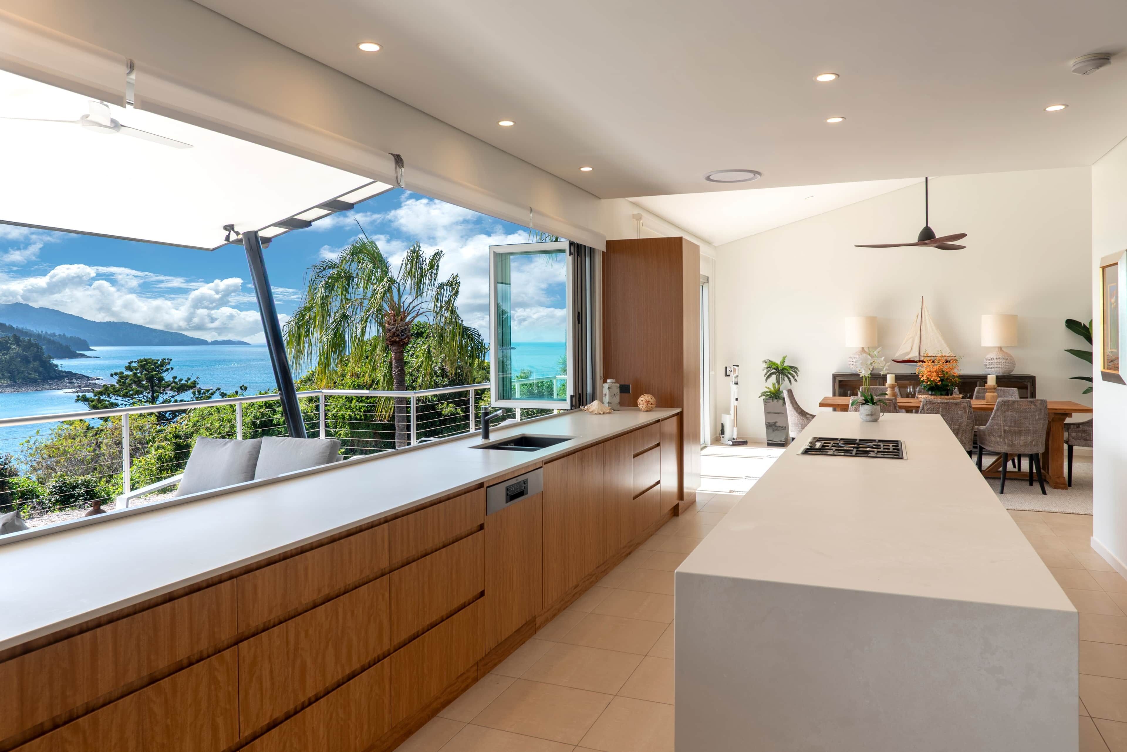 A modern kitchen with a large island, a dining area with a view, and a balcony overlooking the sea.