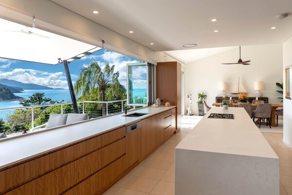 A modern kitchen with a large island, a dining area with a view, and a balcony overlooking the sea.