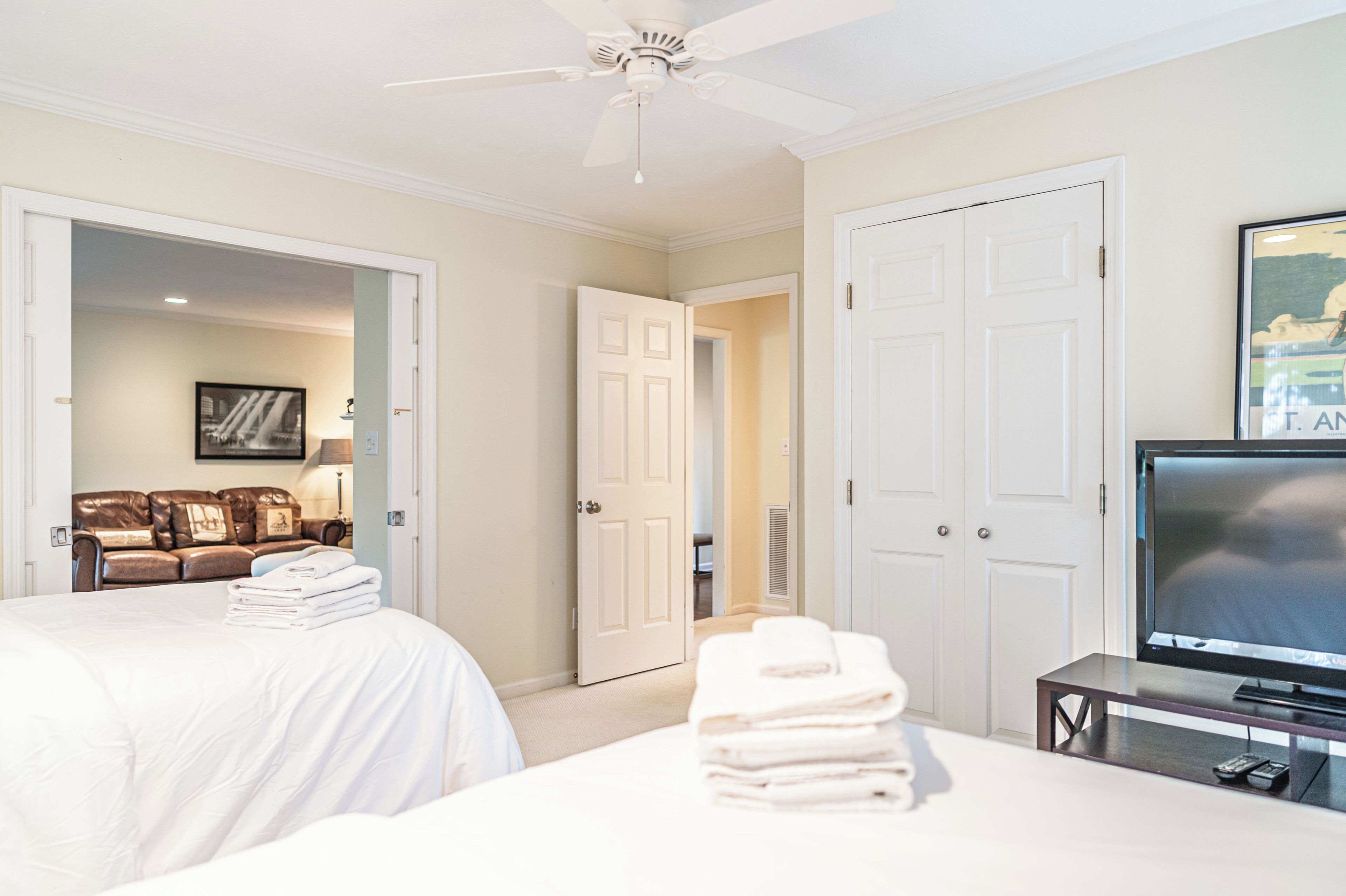 A hotel room with a bed, a television, a seating area with a couch, and a door leading to another room.