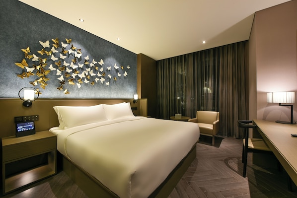 A hotel room with a large bed, a desk, a chair, a wall with butterfly decorations, and a control panel on the nightstand.