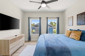A bedroom with a bed, a TV, a ceiling fan, and a window with curtains. - Fall Deals + Snowbird Rates | Near Downtown & Historic St. Andrews Bay (Panama City)