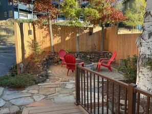A patio area with a stone pathway, wooden deck, and red Adirondack chairs. - Tree house steps from the river (Bend)
