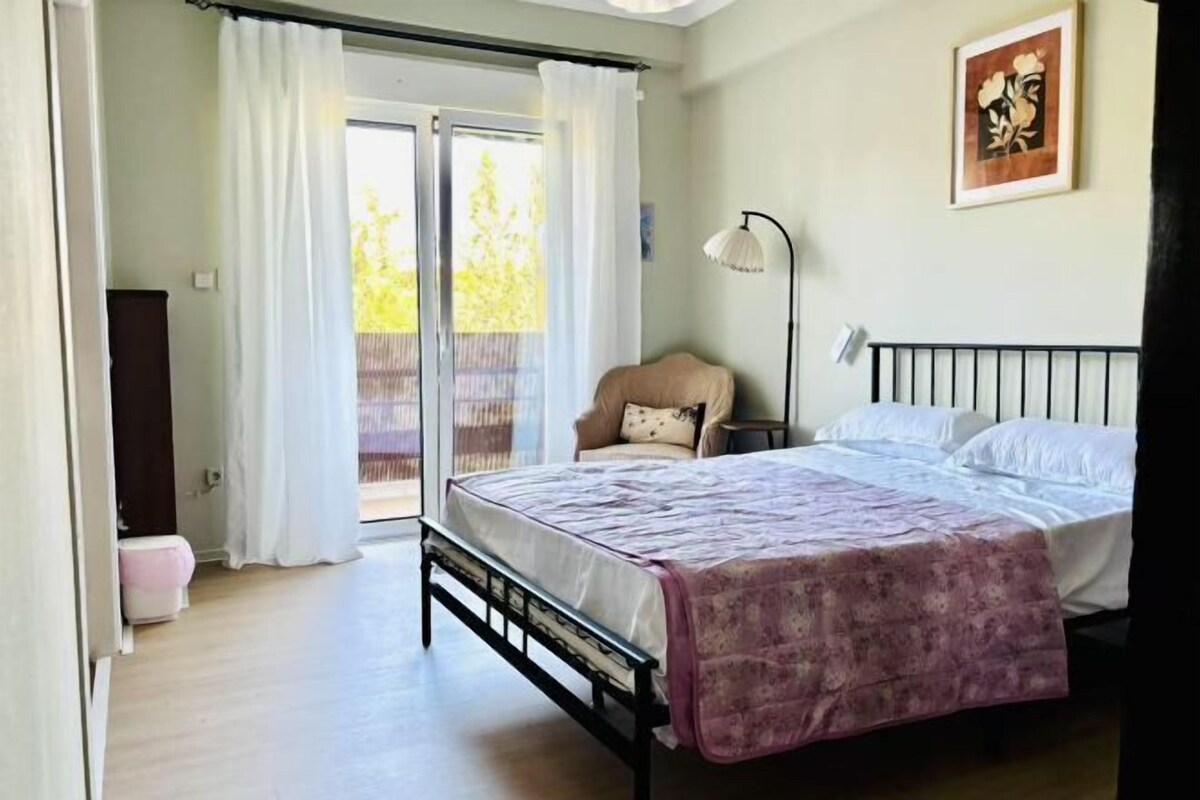 A bedroom with a bed, a chair, a desk, and a window with curtains.