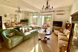 A spacious living room with a large sofa, a smaller armchair, a coffee table, and a television. - Bright City Flat Close to Acropolis Museum (Athens)