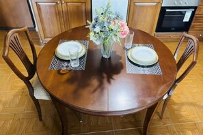 A round wooden dining table with placemats, a vase with flowers, and a glass of water. - Bright City Flat Close to Acropolis Museum (Athens)