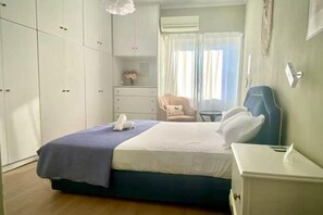 A hotel room with a bed, a bedside table, a chair, a wardrobe, and a window with curtains. - Bright City Flat Close to Acropolis Museum (Athens)