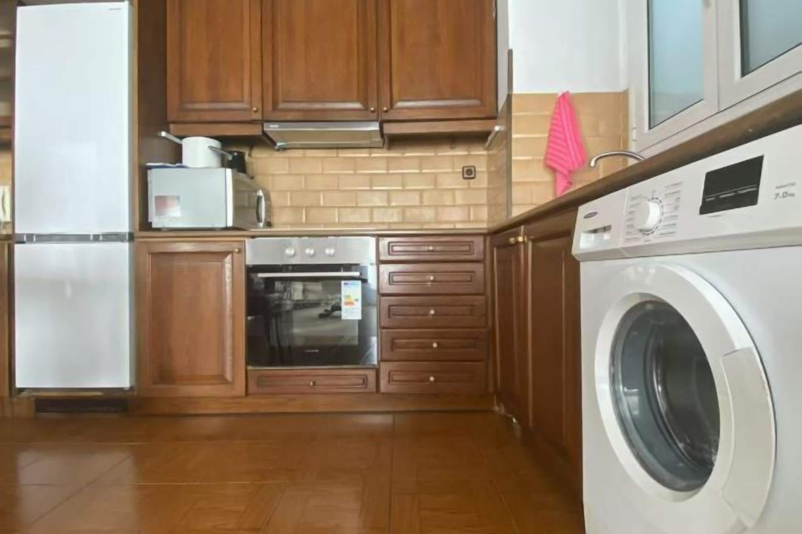 A kitchen with wooden cabinets, a built-in oven, a washing machine, and a microwave.