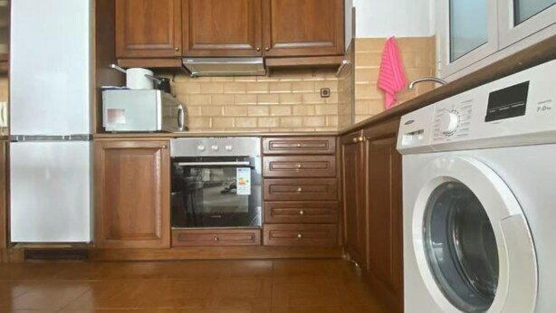 A kitchen with wooden cabinets, a built-in oven, a washing machine, and a microwave. - Bright City Flat Close to Acropolis Museum (Athens)