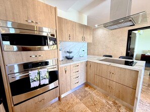 A modern kitchen with stainless steel appliances, marble countertops, and wooden cabinetry. - Luxury Oceanfront 3BR Condo with Huge Terrace, Private Plunge Pool & Ocean Views (Playa del Carmen)
