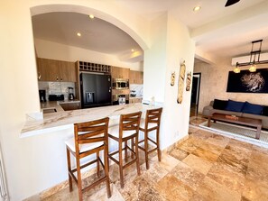 A modern kitchen with a marble countertop, wooden chairs, and a built-in refrigerator. - Luxury Oceanfront 3BR Condo with Huge Terrace, Private Plunge Pool & Ocean Views (Playa del Carmen)