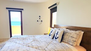 Ein Schlafzimmer mit einem großen Bett, Blick auf den Strand und einer Wanddekoration mit Anker.