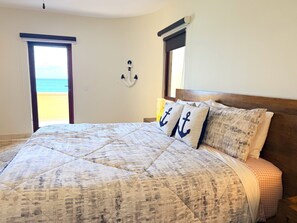 A bedroom with a large bed, a view of the beach, and a wall-mounted anchor decoration. - Luxury Oceanfront 3BR Condo with Huge Terrace, Private Plunge Pool & Ocean Views (Playa del Carmen)