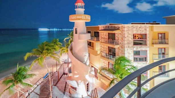 Ein Strandhotel mit einem markanten Leuchtturm, einem Poolbereich mit Palmen und Blick auf den Ozean.